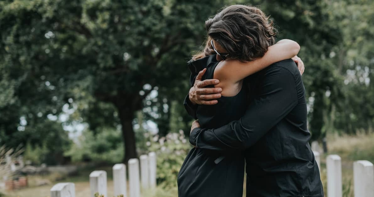 grieving couple hugs in a cemetery | Oliver Law Firm